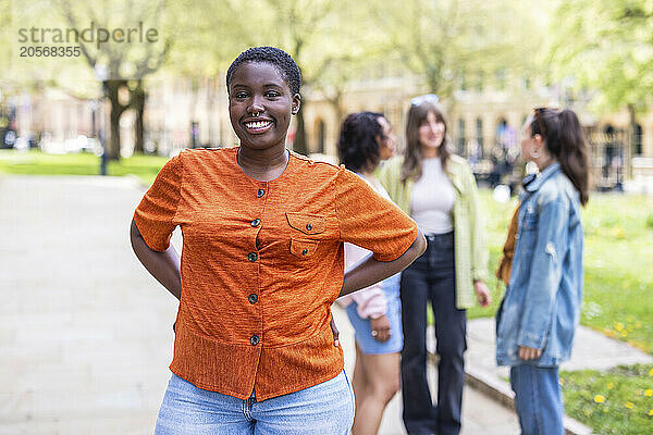 Smiling woman standing with arms akimbo in front of friends