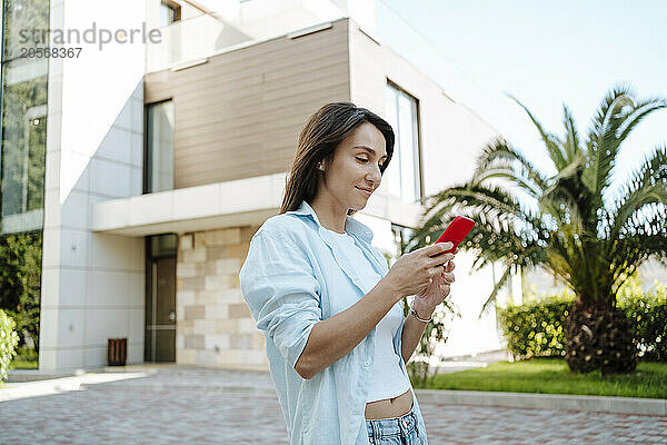 Woman using mobile phone standing in front of house