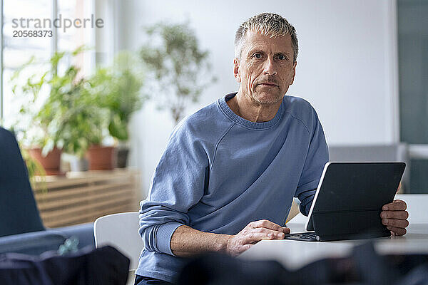 Confident senior man sitting with tablet PC at dining table