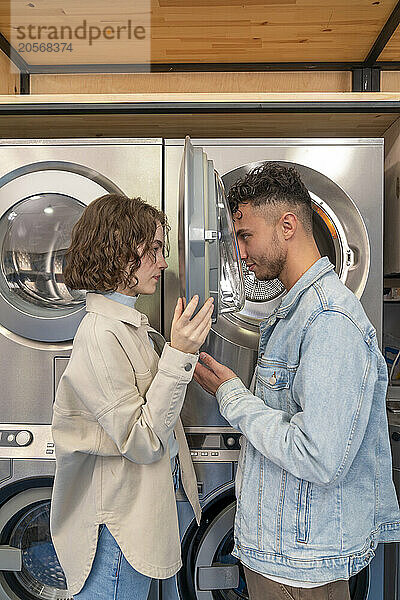 Young couple looking at each other through washing machine glass in laundromat