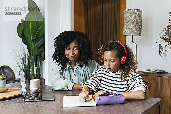 Mother supervising daughter sitting at table doing homework