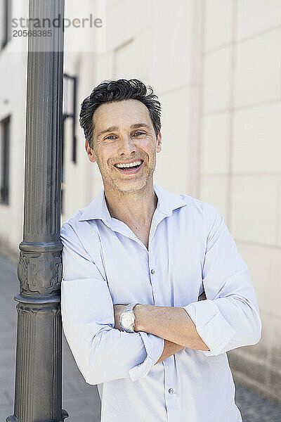 Happy handsome mature businessman with arms crossed leaning on pole