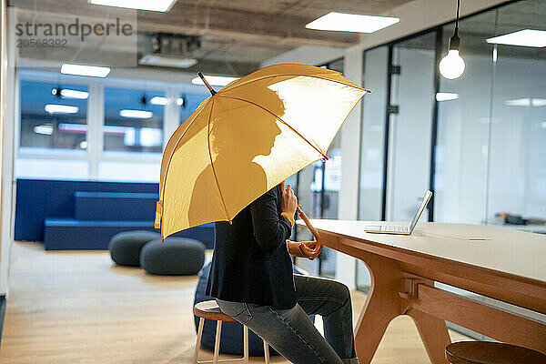 Young businesswoman sitting with yellow umbrella at desk