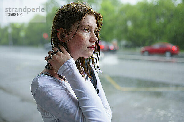 Young woman with hand in hair waiting at bus stop