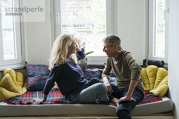 Retired senior couple sitting on alcove window seat at home