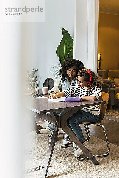 Mother supervising daughter sitting at table doing homework