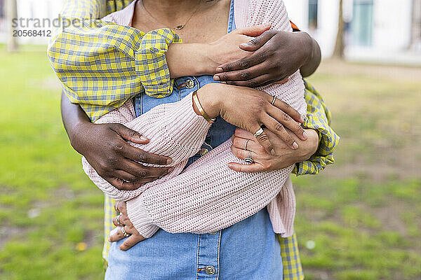 Hands of female friends hugging woman from behind at park