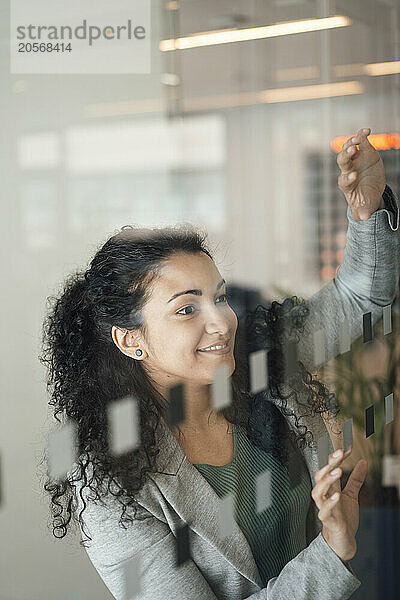 Smiling businesswoman with curly hair standing near glass wall