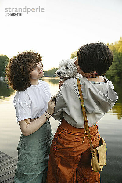 Mother and daughter standing with dog at pier near river