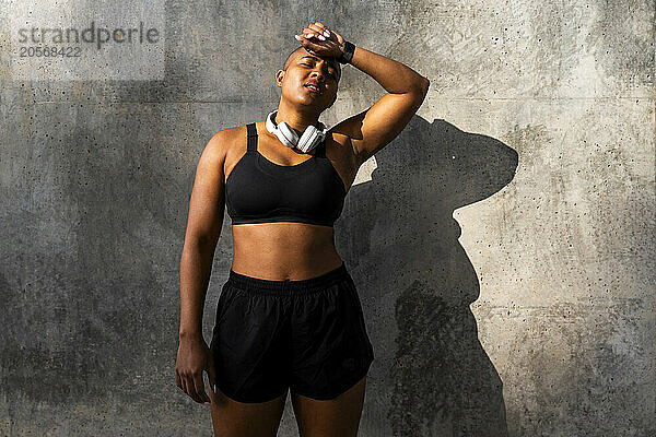 Exhausted sporty muscular woman standing in front of wall