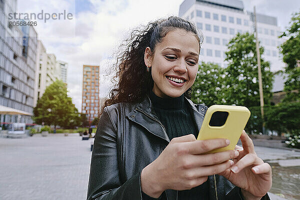 Happy young woman using smart phone in city