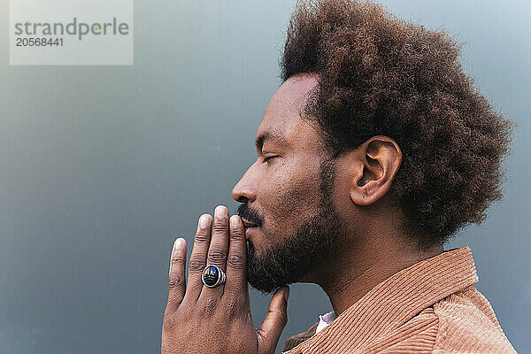 Bearded man with hands clasped and eyes closed against gray background