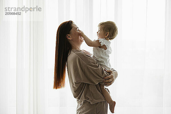 Happy mother carrying daughter by window at home