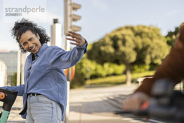 Happy young woman gesturing and standing with electric push scooter at park