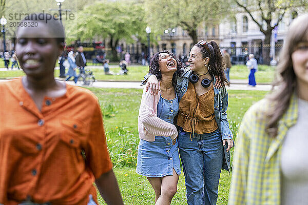 Cheerful women with arms around walking behind friends at park