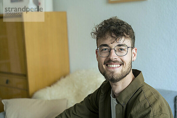 Smiling young handsome man wearing eyeglasses sitting in living room at home