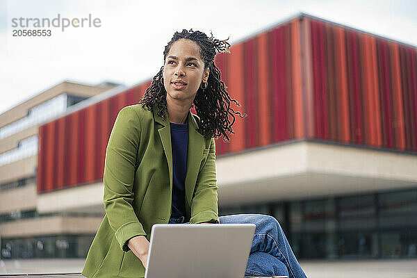 Thoughtful young businesswoman using laptop sitting at office park