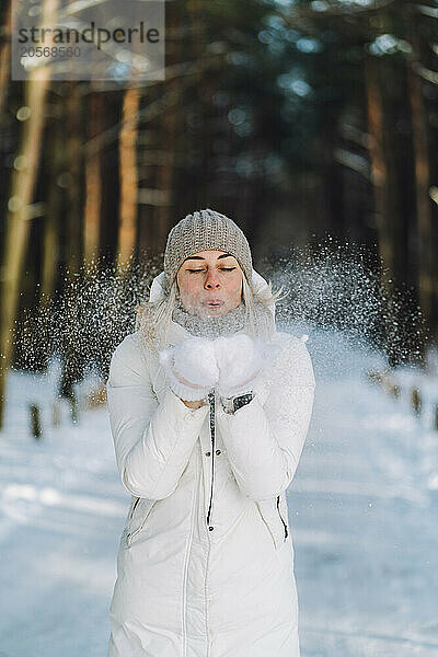 Woman wearing knit hat and blowing snow from hands