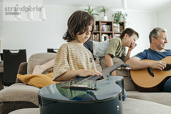 Cute boy touching chords of guitar and father playing Musical instrument at home