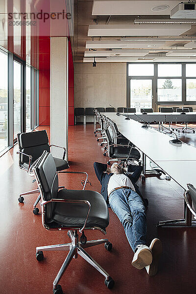 Senior businessman lying on floor amidst chairs relaxing in board room