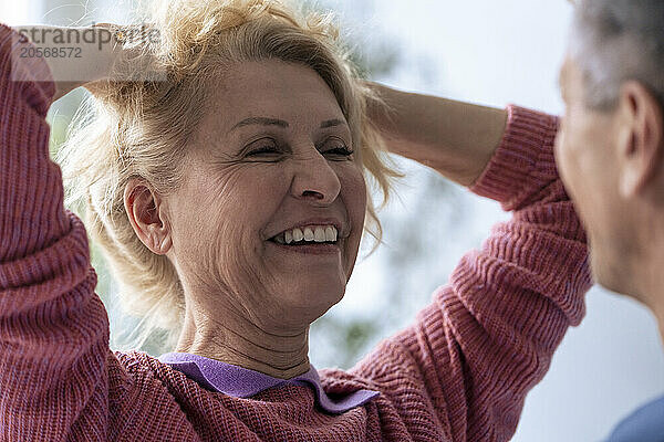 Happy senior woman with hands in hair looking at man