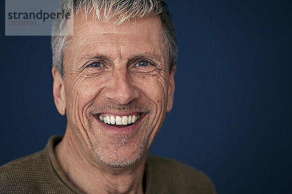 Smiling retired senior man in front of blue wall