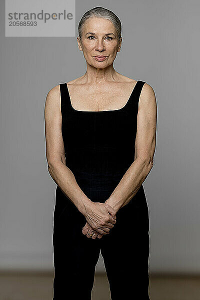 Confident senior woman in black sportswear standing against gray background