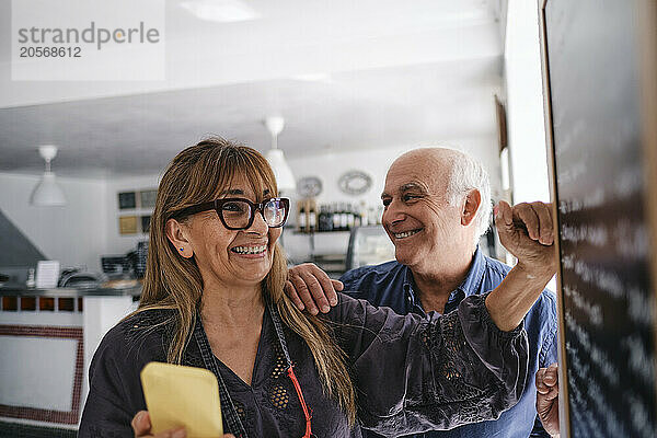 Happy cafe owner with colleague reading menu in coffee shop