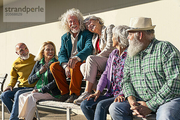 Happy retired women and men sitting together on bench in front of wall