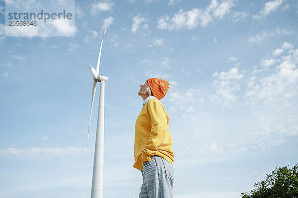 Woman with yellow sweater standing near windmill under blue sky