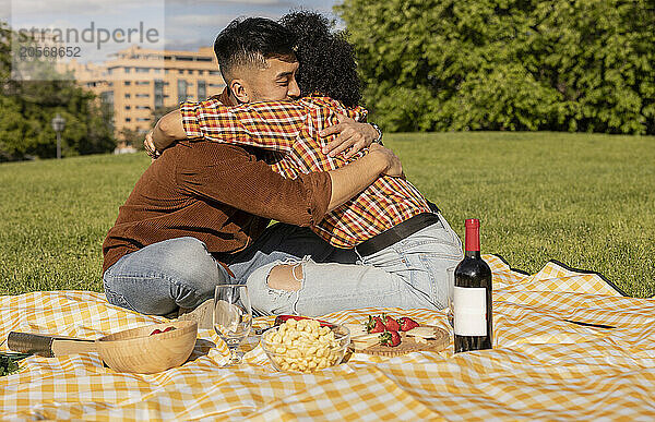 Young man embracing girlfriend and sitting on picnic blanket at park