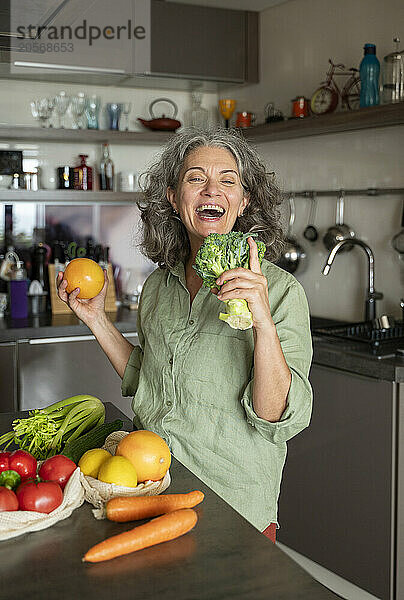 Cheerful woman holding vegetables and enjoying in kitchen