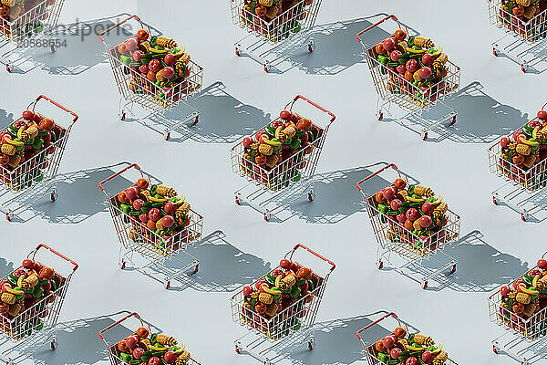 Repetition of shopping cart filled with colorful fruits and vegetables over blue background