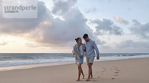 Boyfriend and girlfriend strolling together on sand at beach