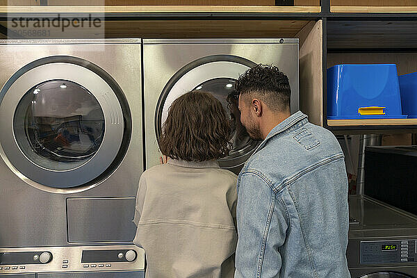 Young couple looking inside washing machine at laundromat