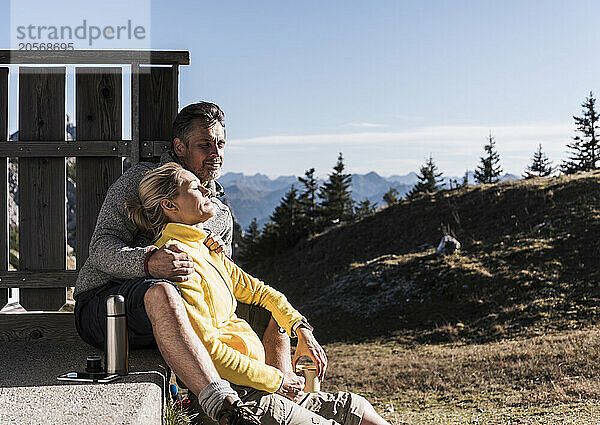 Relaxed woman leaning on boyfriend and sitting near fence in Tyrol