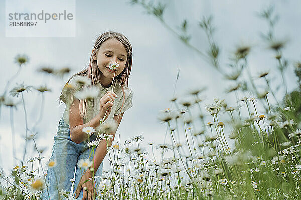 Smiling girl smelling daisy flower at field