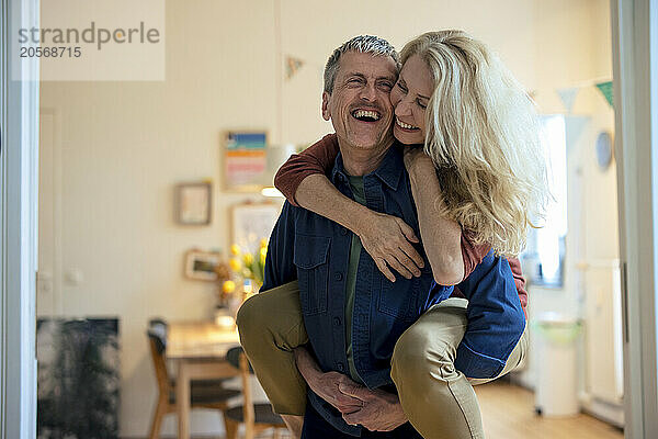 Cheerful senior man piggybacking blond woman at home