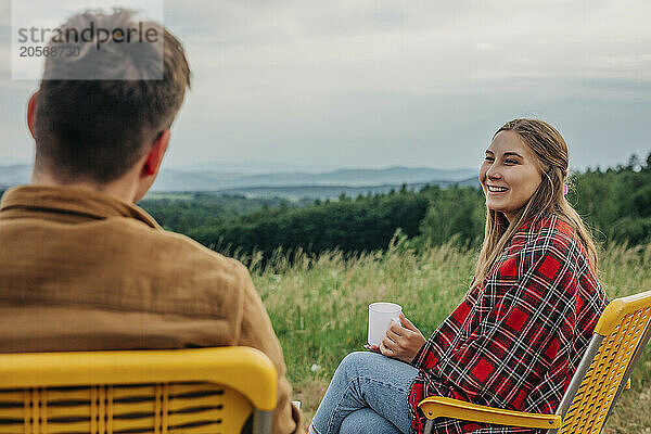 Smiling woman discussing with boyfriend and sitting on chair at mountain of Poland