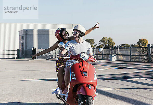 Happy young couple having fun on motor scooter at parking lot