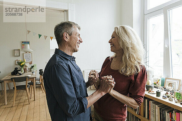 Happy senior couple holding hands standing and talking at home