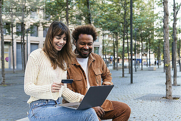 Happy woman with credit card using laptop sitting by boyfriend