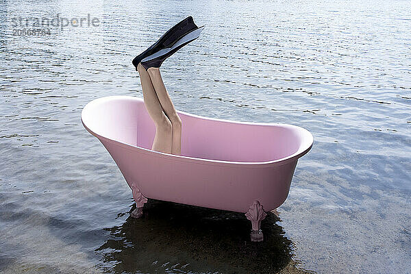 Legs of girl with diving flipper inside pink bathtub in lake