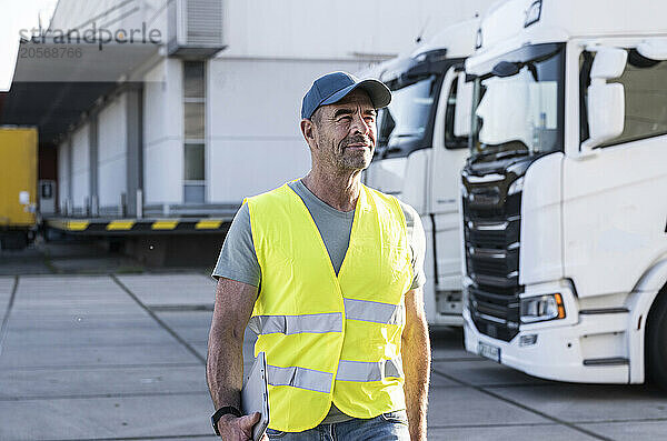 Confident mature manager wearing reflective workwear walking outside warehouse