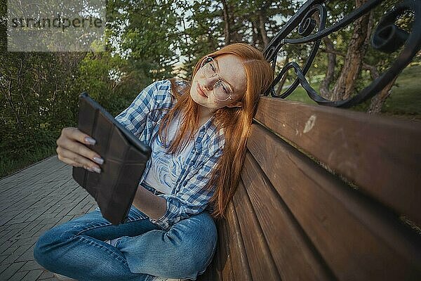 Teenage freelancer using tablet PC and leaning on bench at public park