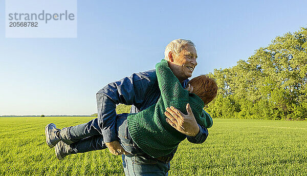 Elderly smiling man holds his grandson in his arms at field