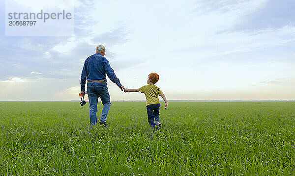 Elderly man and boy holding hands walking on grass