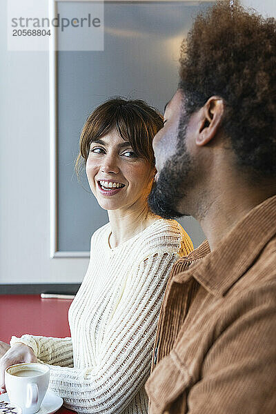 Smiling woman looking at boyfriend sitting in cafe