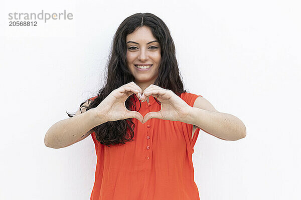 Cheerful woman making heart shape sign with hands against white background