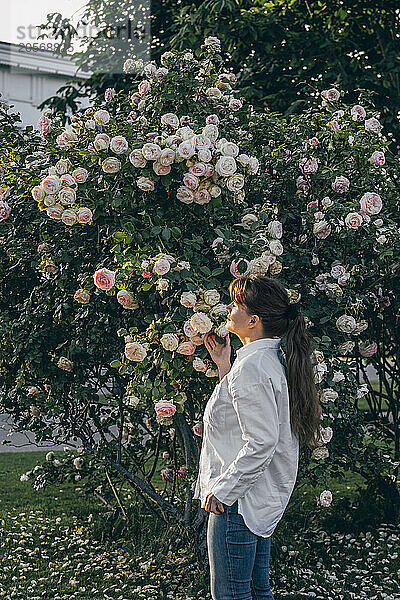 Woman with eyes closed standing near rose tree in garden